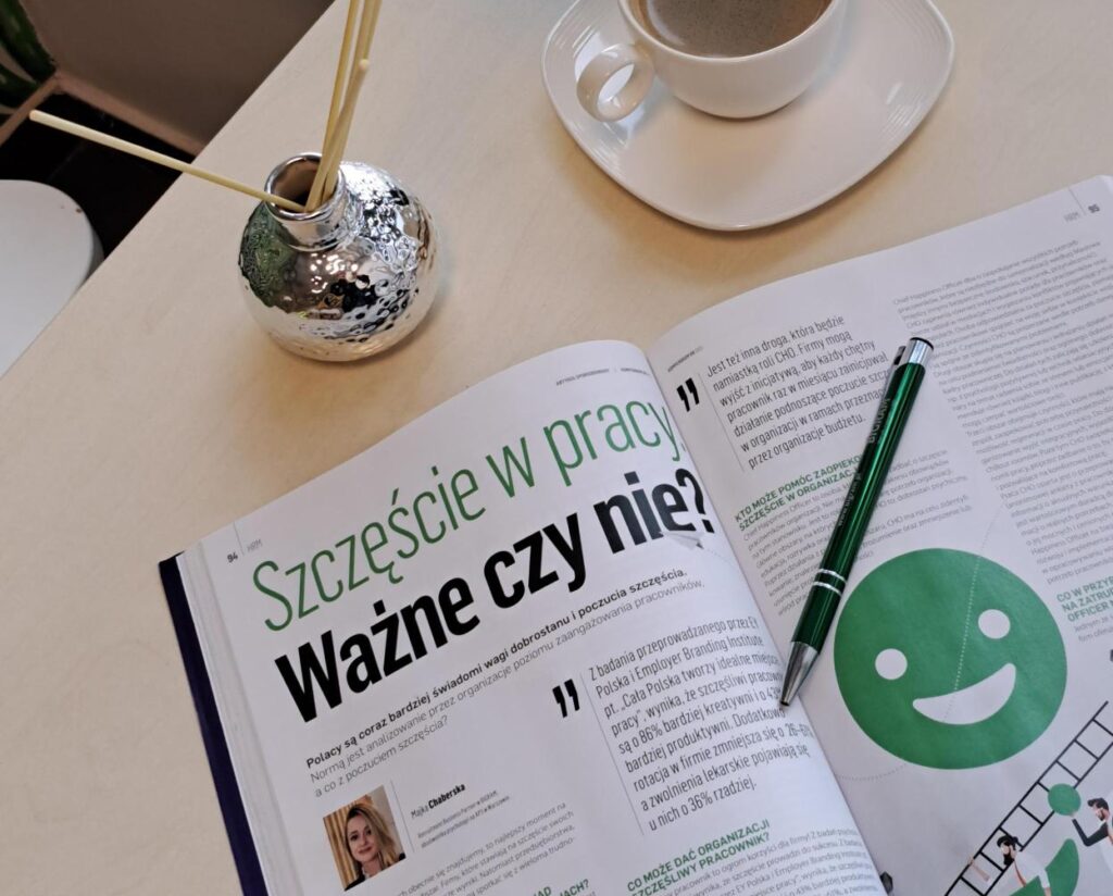Otwarte czasopismo z artykułem o szczęściu w pracy leży na stole, obok stoi filiżanka kawy.